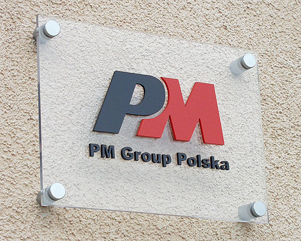 Szyld firmowy wykonany na bezbarwnej pleksi o grubości 8 mm, logo PM zostało wyklejone