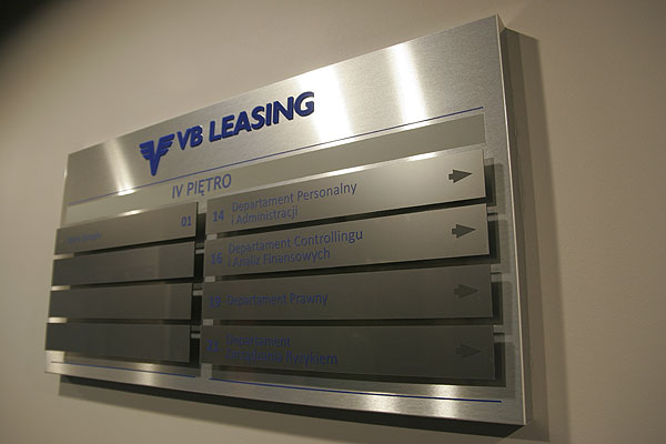 Wypukłe ozdobne logo firmy VB Leasin na tablicy zbiorczej z wymiennymi tabliczkami
opisujacymi działy w biurowcu
